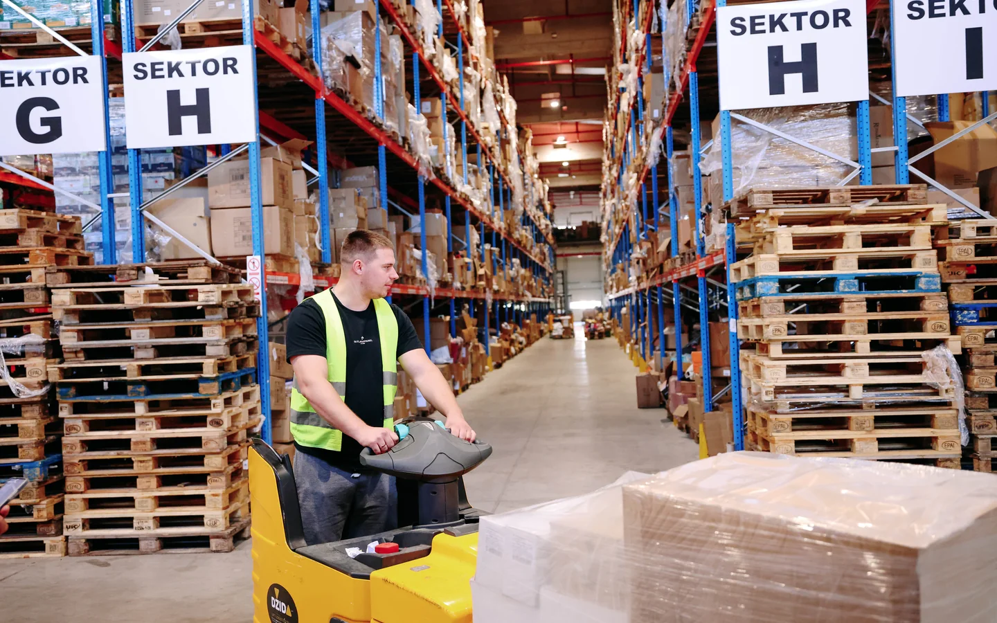 Warehouse operator on an electric pallet truck alongside stock
